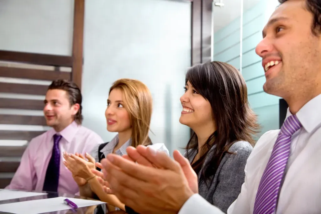 Equipo corporativo aplaudiendo durante presentación profesional utilizando software de Recursos Humanos para fortalecer la comunicación interna.