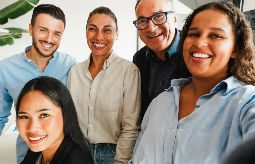 Grupo multicultural sonriente en oficina, utilizando software de Recursos Humanos para mejorar la colaboración organizacional entre empleados